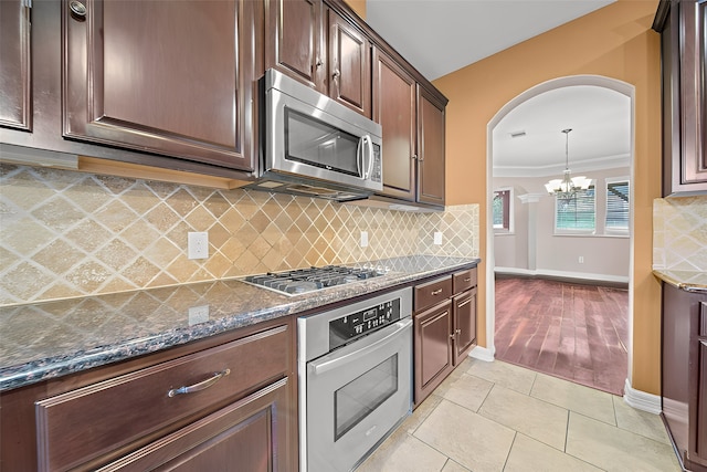 kitchen featuring appliances with stainless steel finishes, dark stone counters, crown molding, decorative backsplash, and a chandelier