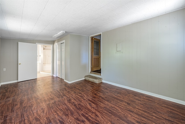 unfurnished room featuring wooden walls and dark wood-type flooring