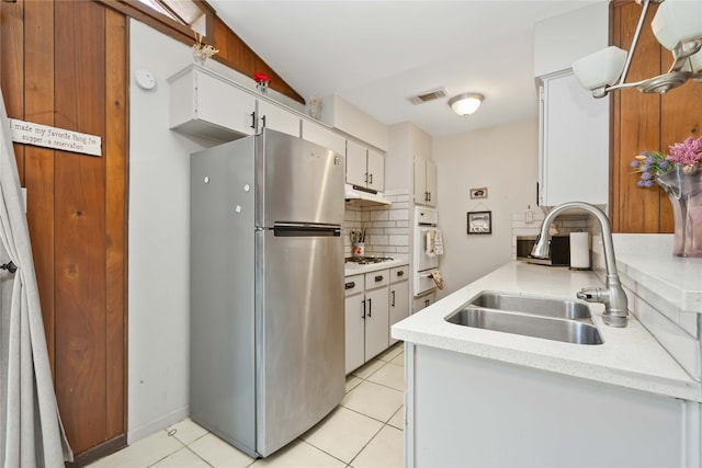 kitchen with sink, tasteful backsplash, oven, white cabinetry, and stainless steel refrigerator