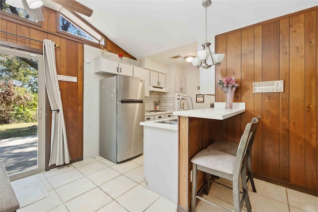 kitchen featuring wood walls, stainless steel fridge, decorative light fixtures, lofted ceiling, and white cabinets