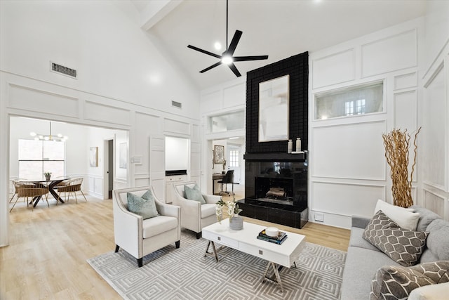 living room with ceiling fan with notable chandelier, light hardwood / wood-style floors, high vaulted ceiling, and a large fireplace