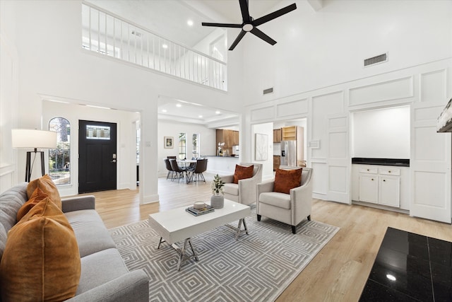 living room featuring high vaulted ceiling, ceiling fan, beamed ceiling, and light hardwood / wood-style flooring