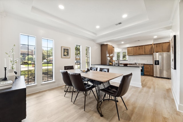 dining room featuring ornamental molding, a tray ceiling, and light hardwood / wood-style floors