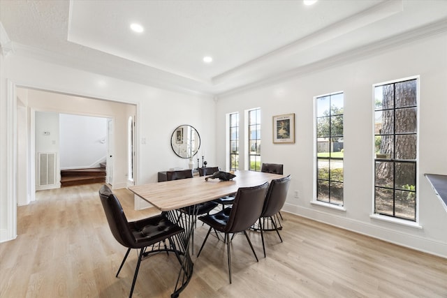 dining space featuring crown molding, a tray ceiling, and light hardwood / wood-style flooring