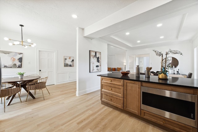 kitchen with light wood-type flooring, stainless steel microwave, a notable chandelier, hanging light fixtures, and a textured ceiling