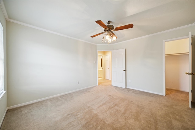 unfurnished bedroom featuring ceiling fan, a closet, crown molding, a walk in closet, and light colored carpet