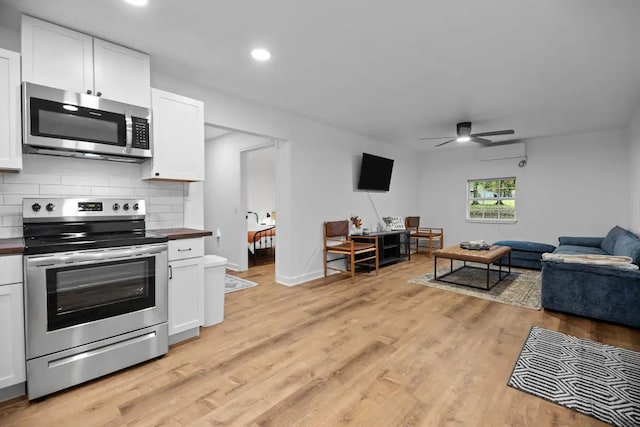 kitchen with light hardwood / wood-style floors, white cabinets, a wall mounted AC, and stainless steel appliances