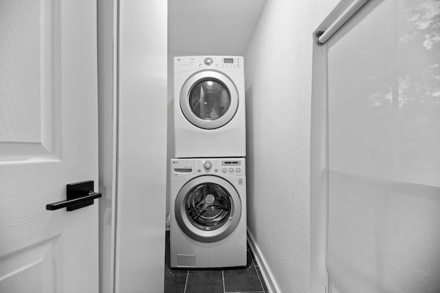 laundry area with stacked washer / drying machine and dark tile patterned flooring