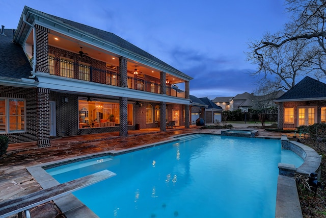 pool at dusk with an in ground hot tub, a diving board, and a patio area