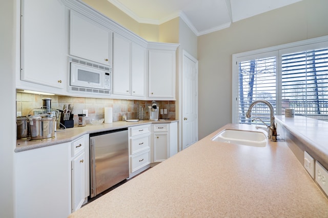 kitchen with stainless steel refrigerator, white microwave, sink, ornamental molding, and white cabinets