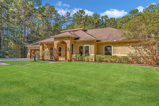 mediterranean / spanish house with a front yard, stone siding, an attached garage, and stucco siding