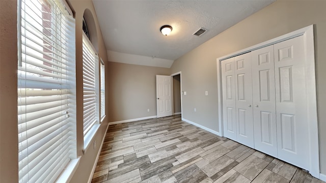 unfurnished bedroom featuring a textured ceiling, light wood-type flooring, a closet, and multiple windows