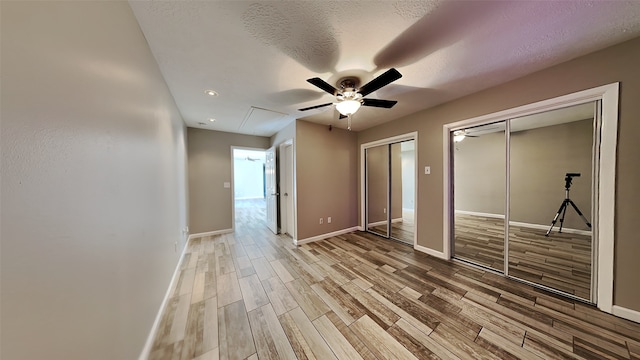 unfurnished bedroom with ceiling fan, a textured ceiling, light wood-type flooring, and two closets