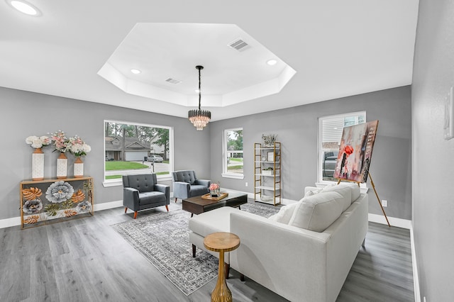 living room featuring an inviting chandelier, a raised ceiling, and hardwood / wood-style floors