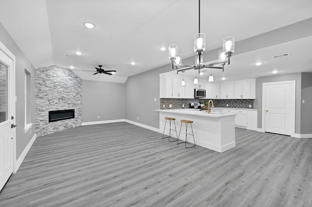 kitchen featuring light wood-type flooring, pendant lighting, vaulted ceiling, stainless steel appliances, and white cabinetry