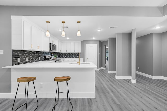 kitchen with kitchen peninsula, decorative light fixtures, light hardwood / wood-style flooring, white cabinetry, and appliances with stainless steel finishes