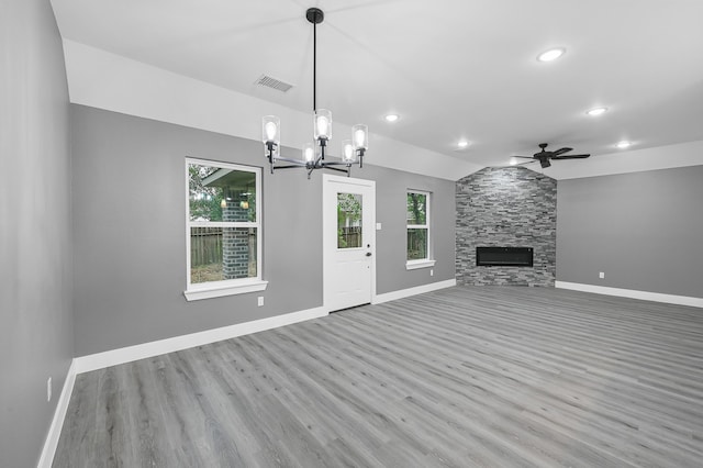 unfurnished living room with ceiling fan with notable chandelier, a stone fireplace, light hardwood / wood-style flooring, and lofted ceiling