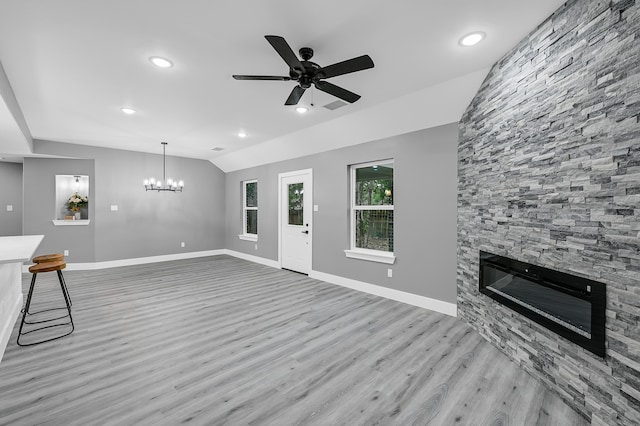 unfurnished living room with ceiling fan with notable chandelier, lofted ceiling, a fireplace, and light wood-type flooring