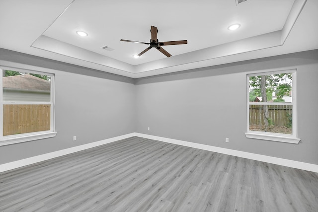 spare room featuring ceiling fan, light wood-type flooring, and a tray ceiling