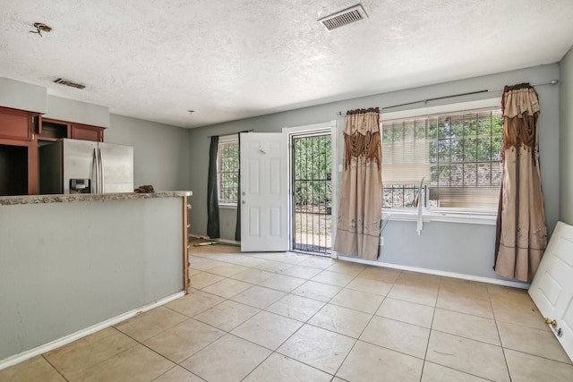 interior space featuring light tile patterned floors, stainless steel fridge with ice dispenser, a textured ceiling, and a wealth of natural light