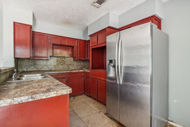 kitchen featuring sink, stainless steel refrigerator with ice dispenser, decorative backsplash, light tile patterned floors, and a textured ceiling