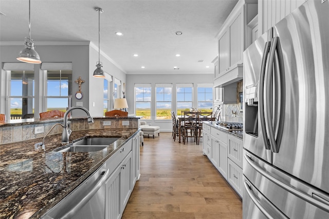 kitchen with white cabinets, sink, decorative light fixtures, appliances with stainless steel finishes, and light wood-type flooring
