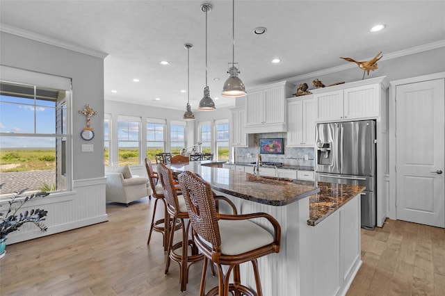 kitchen featuring light wood-type flooring, dark stone countertops, hanging light fixtures, stainless steel fridge with ice dispenser, and white cabinetry