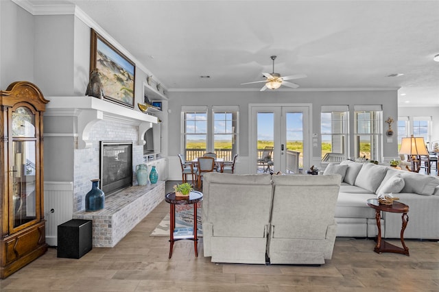 living room with light wood-type flooring, ceiling fan, french doors, a fireplace, and crown molding