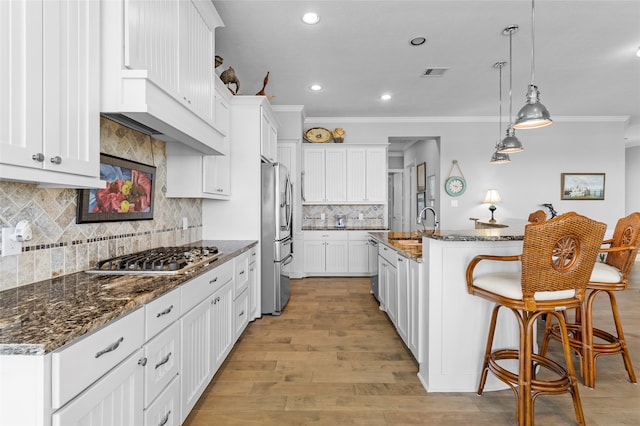 kitchen with light wood-type flooring, a kitchen island with sink, stainless steel appliances, white cabinetry, and ornamental molding