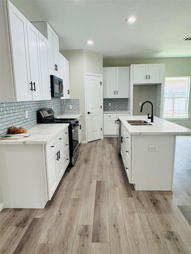 kitchen featuring white cabinetry, sink, light hardwood / wood-style floors, stainless steel appliances, and a center island with sink