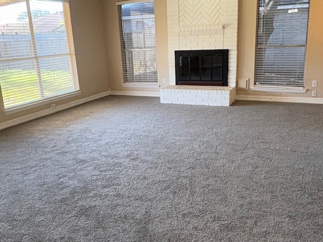 unfurnished living room with a brick fireplace, carpet, and plenty of natural light