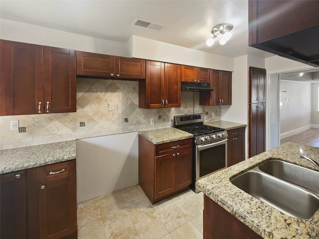 kitchen with light stone countertops, sink, gas stove, and tasteful backsplash