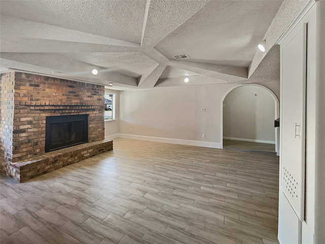 unfurnished living room with a fireplace, light hardwood / wood-style floors, and a textured ceiling