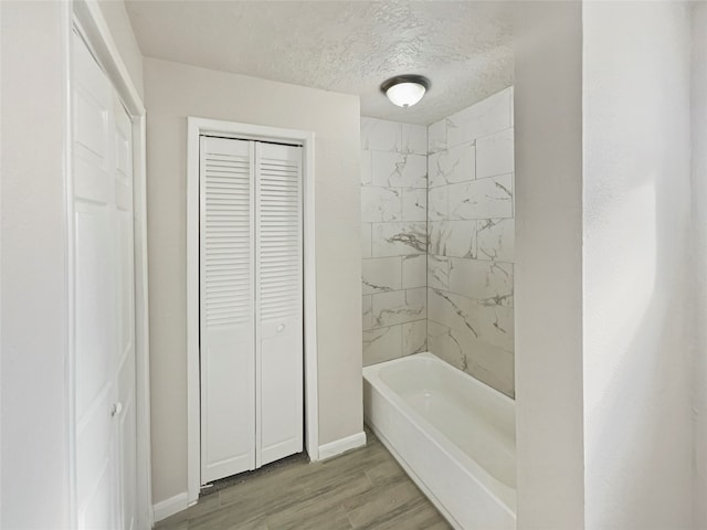 bathroom featuring wood-type flooring, tiled shower / bath, and a textured ceiling