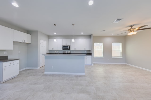 kitchen with ceiling fan, an island with sink, sink, decorative light fixtures, and white cabinetry