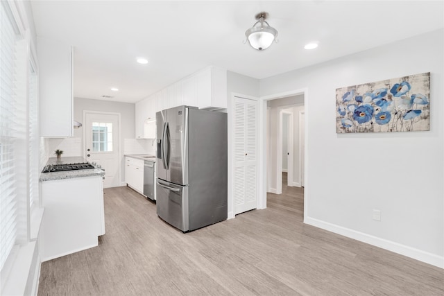 kitchen featuring tasteful backsplash, light hardwood / wood-style flooring, white cabinetry, appliances with stainless steel finishes, and light stone countertops