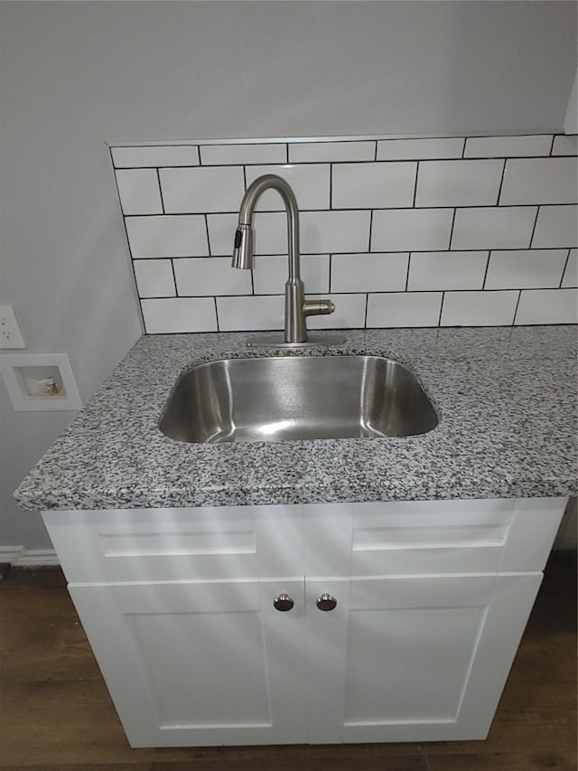 details with light stone counters, a sink, backsplash, and dark wood-style floors