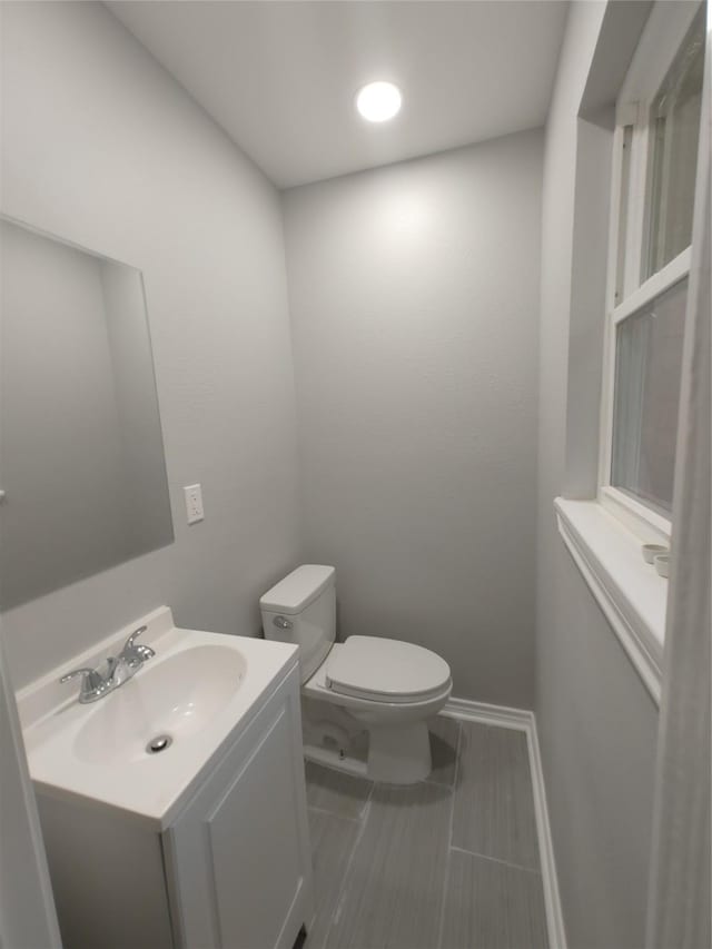 half bath featuring baseboards, vanity, and toilet