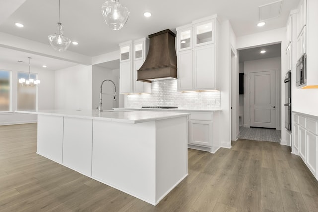 kitchen with a center island with sink, custom exhaust hood, and white cabinets