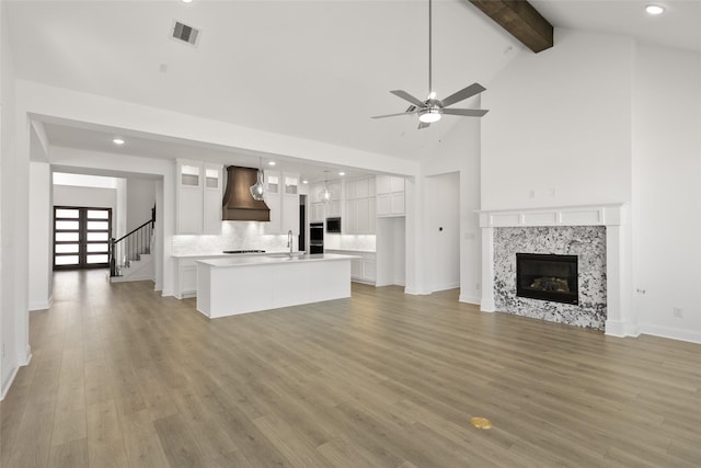 unfurnished living room with light hardwood / wood-style floors, ceiling fan, beamed ceiling, a tiled fireplace, and sink