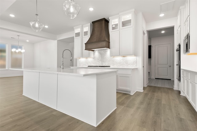 kitchen with white cabinets, a kitchen island with sink, and custom range hood