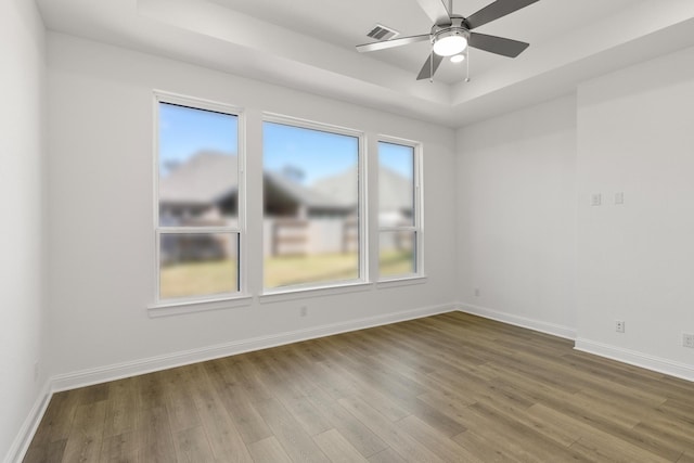 empty room with ceiling fan, wood-type flooring, and a tray ceiling