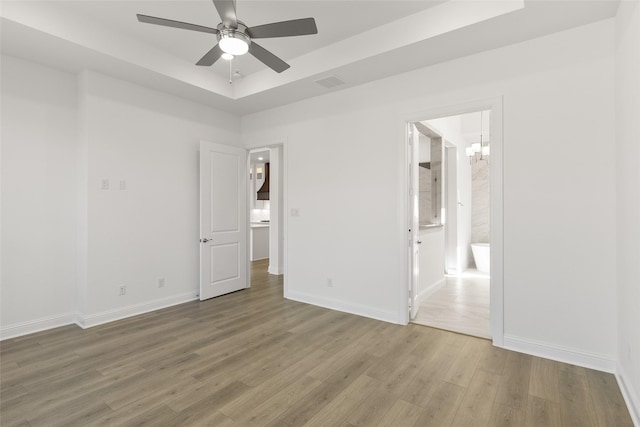 unfurnished bedroom with ensuite bath, wood-type flooring, a tray ceiling, and ceiling fan