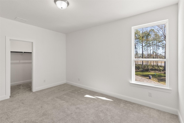 unfurnished bedroom featuring a walk in closet, a closet, light carpet, and baseboards