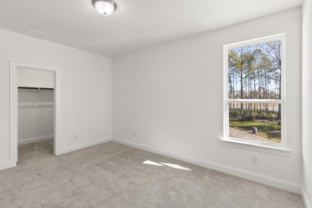 unfurnished bedroom with a closet, light colored carpet, a spacious closet, and baseboards