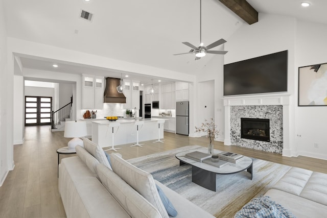 living room featuring visible vents, light wood-style flooring, a premium fireplace, high vaulted ceiling, and beamed ceiling