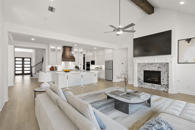 living area featuring beam ceiling, visible vents, a high end fireplace, high vaulted ceiling, and light wood-type flooring