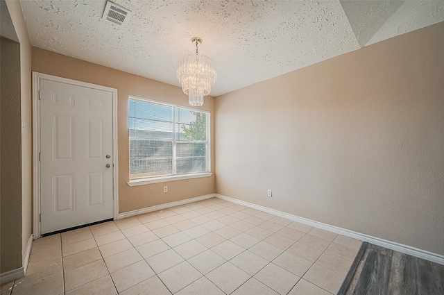 tiled empty room featuring a chandelier and a textured ceiling