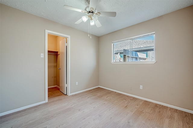 unfurnished bedroom featuring a spacious closet, ceiling fan, light hardwood / wood-style flooring, a textured ceiling, and a closet