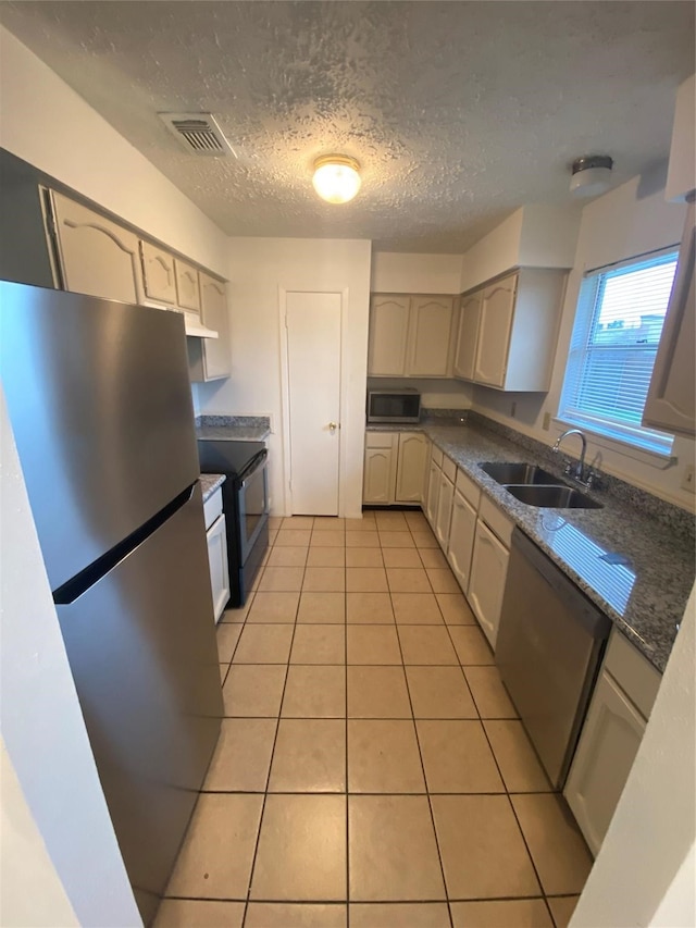 kitchen with sink, dark stone countertops, light tile patterned floors, a textured ceiling, and appliances with stainless steel finishes